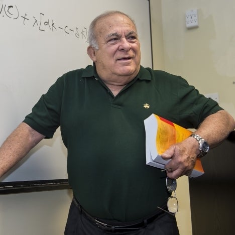 An economics professor stands in front of a whiteboard.